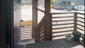 Vista desde un balcón con barandilla de metal, sobre un estacionamiento con varios vehículos y un edificio con señalización.