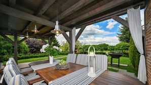 Een terras buiten met houten vloer, gestreept zitmeubilair met kussens en hangende hanglampen.