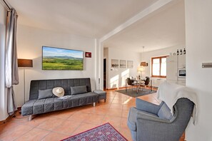 Un salon comprenant un canapé, un fauteuil, un coin repas et une cuisine.
