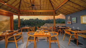 Un restaurante con mobiliario de madera, techo de paja y cuadros en las paredes.
