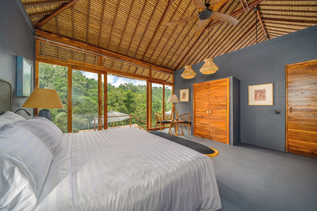 A bedroom with a large bed, wooden doors, and a view of the outdoors.