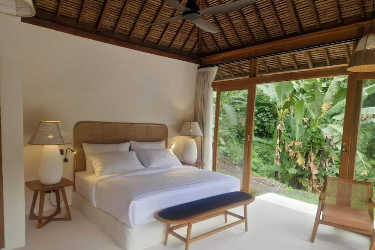 A bedroom with a bed, bedside lamps, a bench, and a chair.