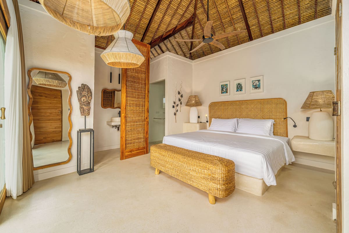 A spacious bedroom with a large bed, a ceiling fan, and a woven bench.