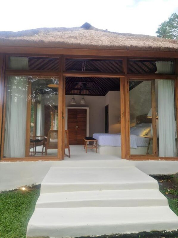A modern guest room with a large sliding glass door, a bed, a small table, and a chair.