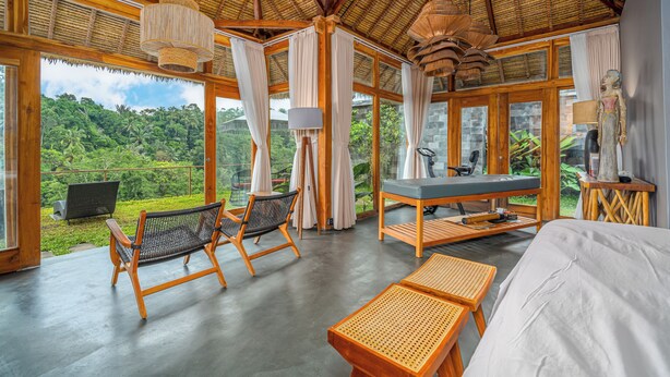 Una habitación amplia con una cama grande, dos sillas, una mesa y vistas a exuberante follaje.
