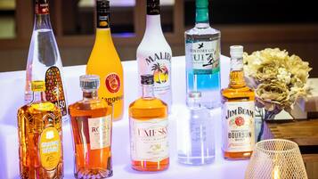 A variety of liquor bottles on a table with a decorative lamp and flowers.