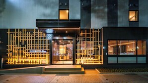 Una entrada de hotel moderna con fachada geométrica, señalización iluminada y acceso visible.