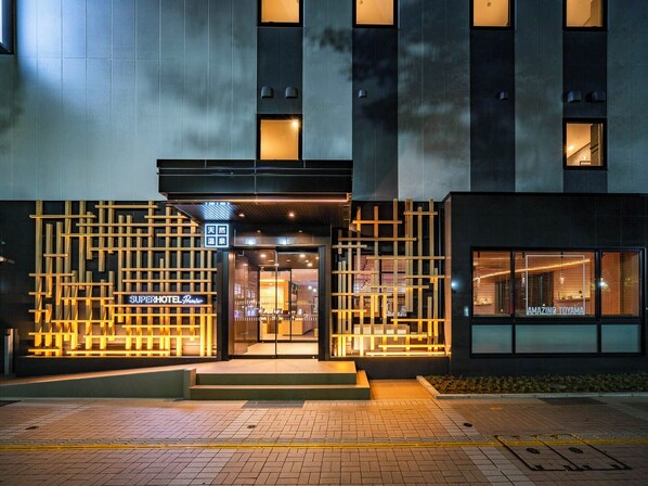 A modern hotel entrance with a geometric facade, illuminated signage, and a visible entrance.