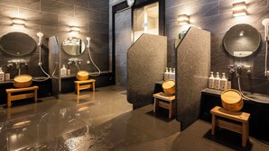 Un baño moderno con paredes de piedra oscura, varios lavamanos y taburetes de madera.
