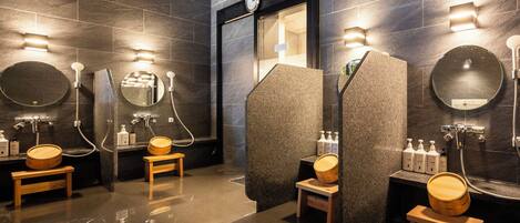 A modern bathroom with dark stone walls, multiple sinks, and wooden stools.
