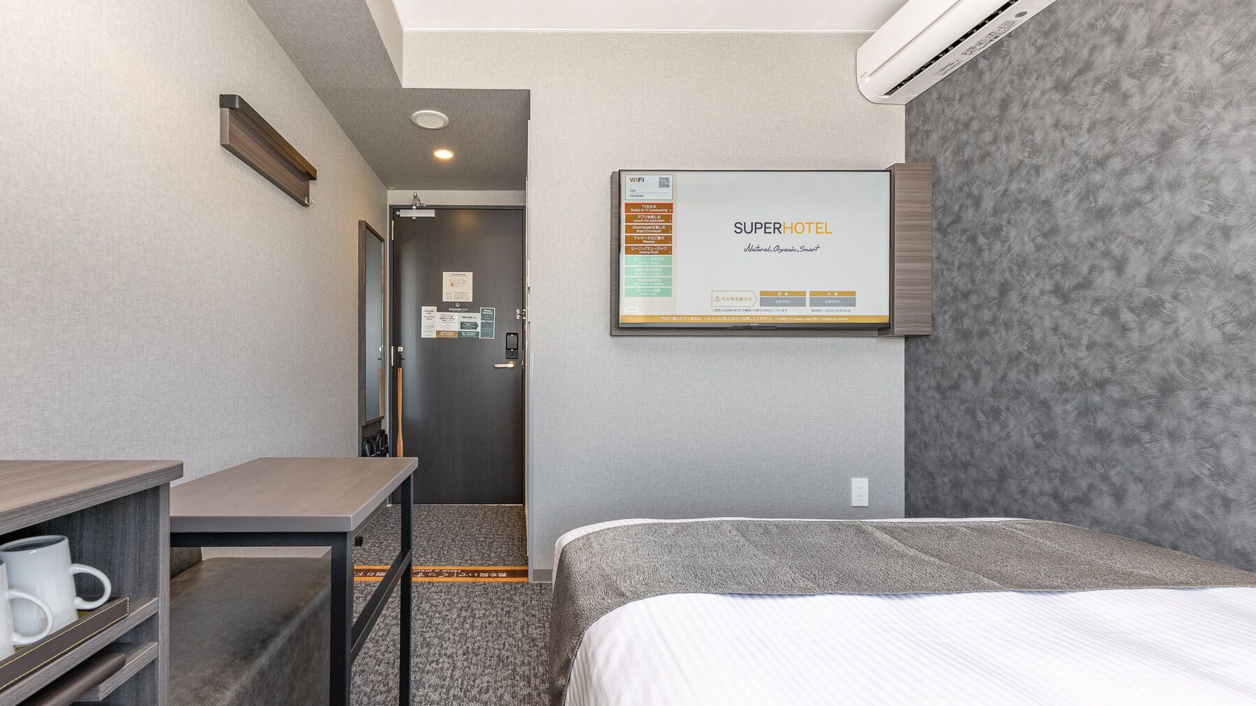 Une chambre d’hôtel équipée d’un lit, d’un bureau, d’une chaise, d’une machine à café et d’un climatiseur fixé au mur.