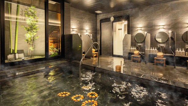 Un spa moderno con una piscina grande climatizada, taburetes de madera y una planta de bambú.