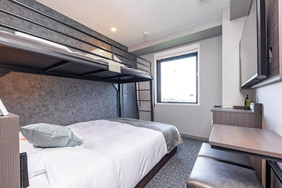 Una habitación de hotel moderna con literas, un escritorio y una ventana que ofrece vistas.