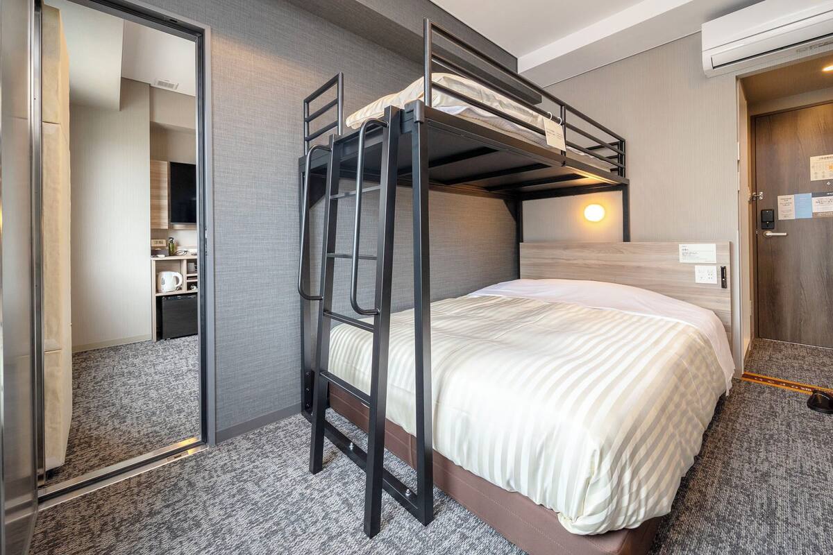Una cama individual superpuesta con escalera, una mesita de noche, un espejo y un aire acondicionado instalado en la pared.