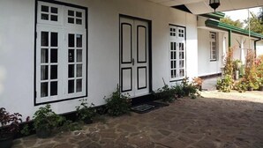 A covered outdoor area with a stone floor, white walls, and multiple windows with black frames. - Silver Meir Bungalow (Nuwara Eliya)