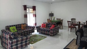 A living room with two plaid sofas, a dining table with chairs, and a window with curtains. - Silver Meir Bungalow (Nuwara Eliya)
