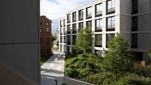 A modern building with multiple floors, large windows, and a paved pathway leading to a green area with trees.