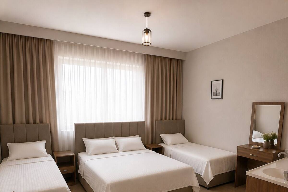 A hotel room with three beds, a sofa, a desk with a mirror, and a hanging light fixture.