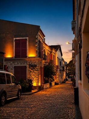 A cobblestone street with buildings, a parked car, and a flag. - Viyana Otel (Cesme)