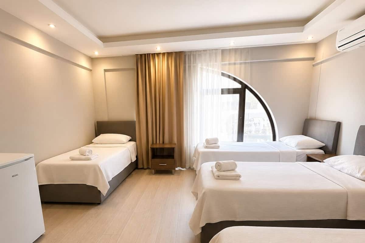 A hotel room with two beds, a small bedside table, a wardrobe, and a large window with curtains.