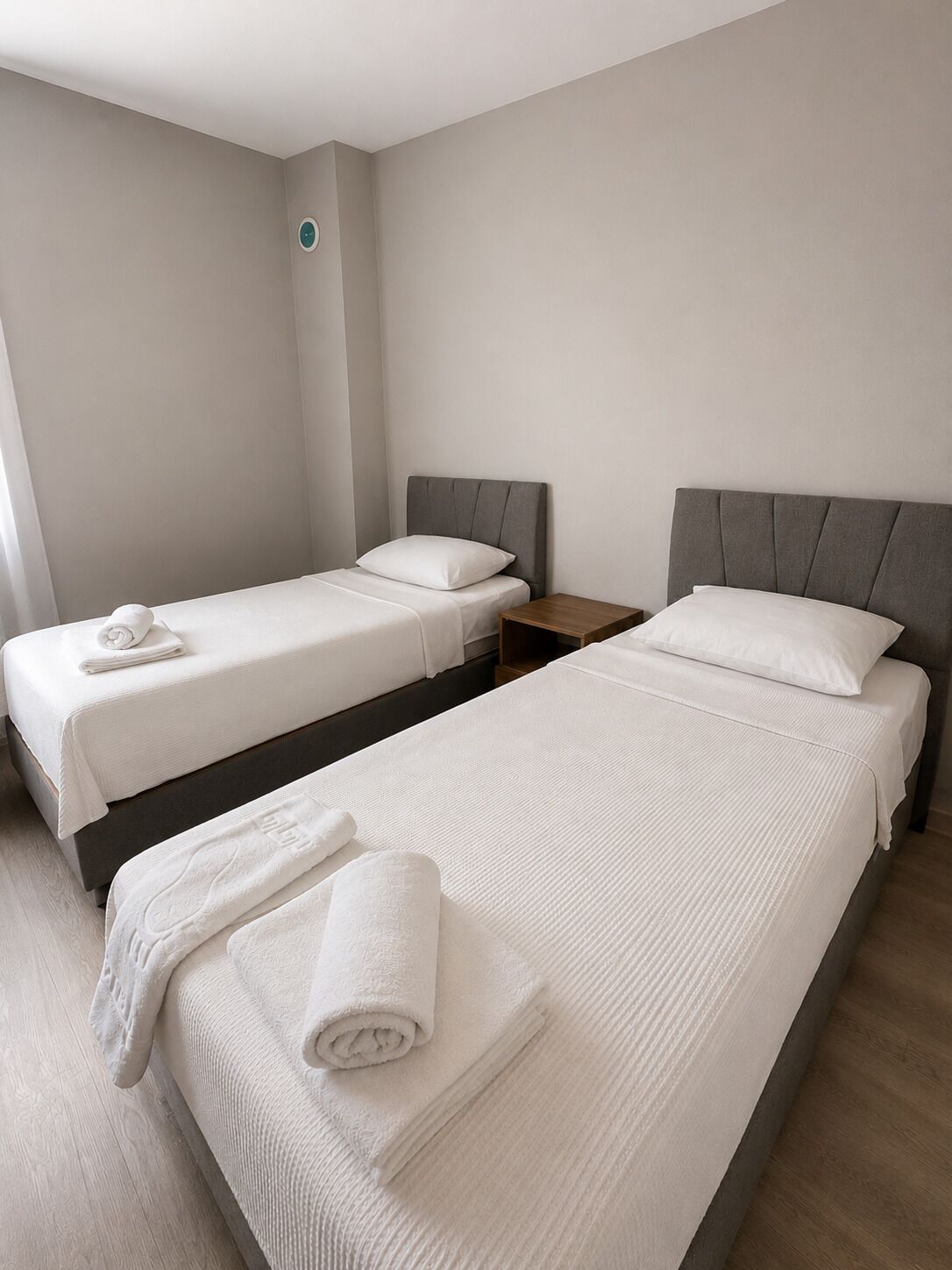 Habitación de hotel con dos camas, cada una con una almohada y una toalla enrollada.