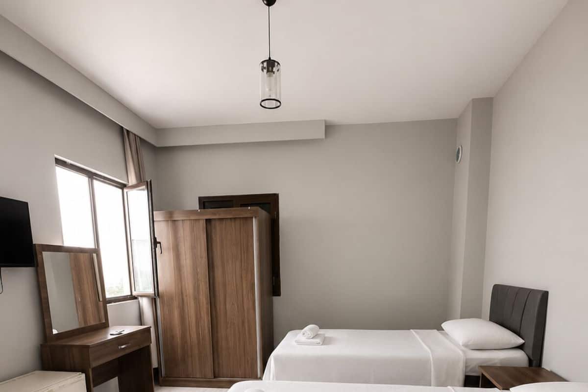 A modern hotel room with two beds, a desk, a wardrobe, and a TV.
