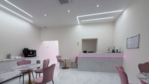 Una habitación moderna y luminosa con suelo de mármol, sillas rosas y un mostrador de recepción.