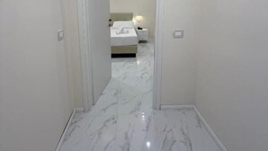 Un pasillo con piso de mármol que conduce a un dormitorio con cama y mesita de noche.