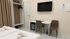 Habitación de hotel con dos camas, un escritorio, una silla, un televisor y un armario.