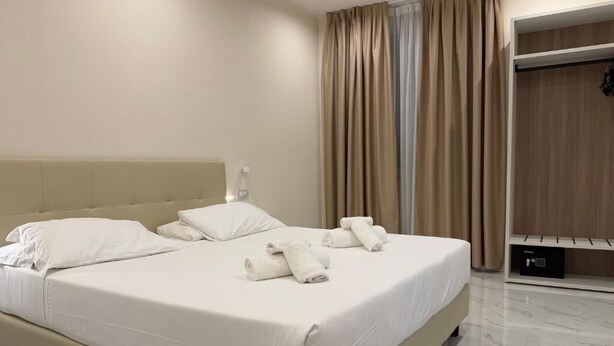 Una cama bien hecha con sábanas y toallas blancas, cabecera y un armario de madera con espejo.