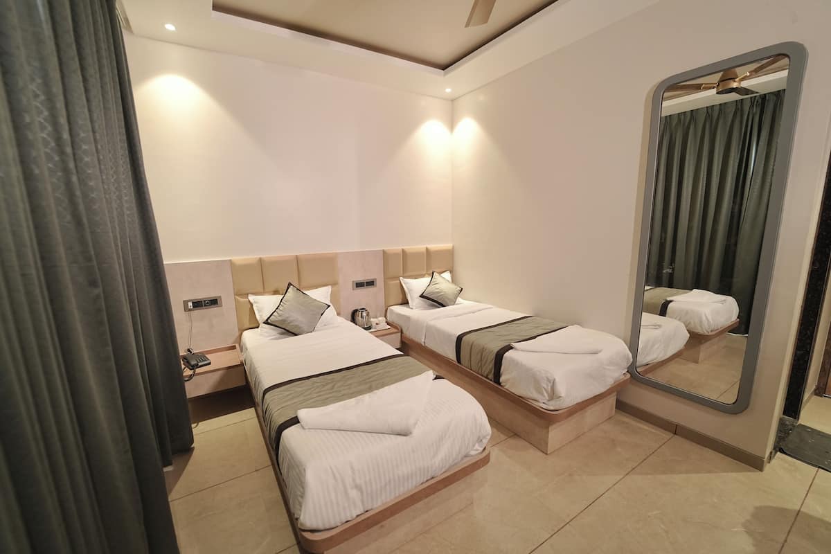 A hotel room with two single beds, a large mirror, a bedside table with a lamp, and a power outlet.
