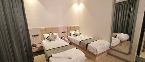 A hotel room with two single beds, a large mirror, a bedside table with a lamp, and a power outlet.