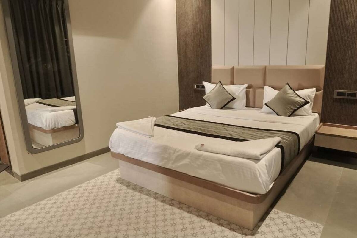 A modern hotel room with a large bed, a mirror, and a wooden headboard.