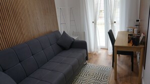 A modern living room with a dark grey sofa, a wooden floor, and a small wooden table with a radio. - Sava House Entire apartment newly renovated. Cozy and quiet! (Roma)