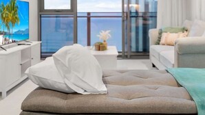 Een moderne slaapkamer met een groot bed, een televisie, een balkon met uitzicht op zee en een stadsgezicht.