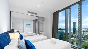 Een hotelkamer met twee bedden, een groot raam met uitzicht op de stad, een kledingkast en een spiegel.