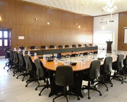 Un salón de conferencias con una larga mesa, varias sillas y un atril.
