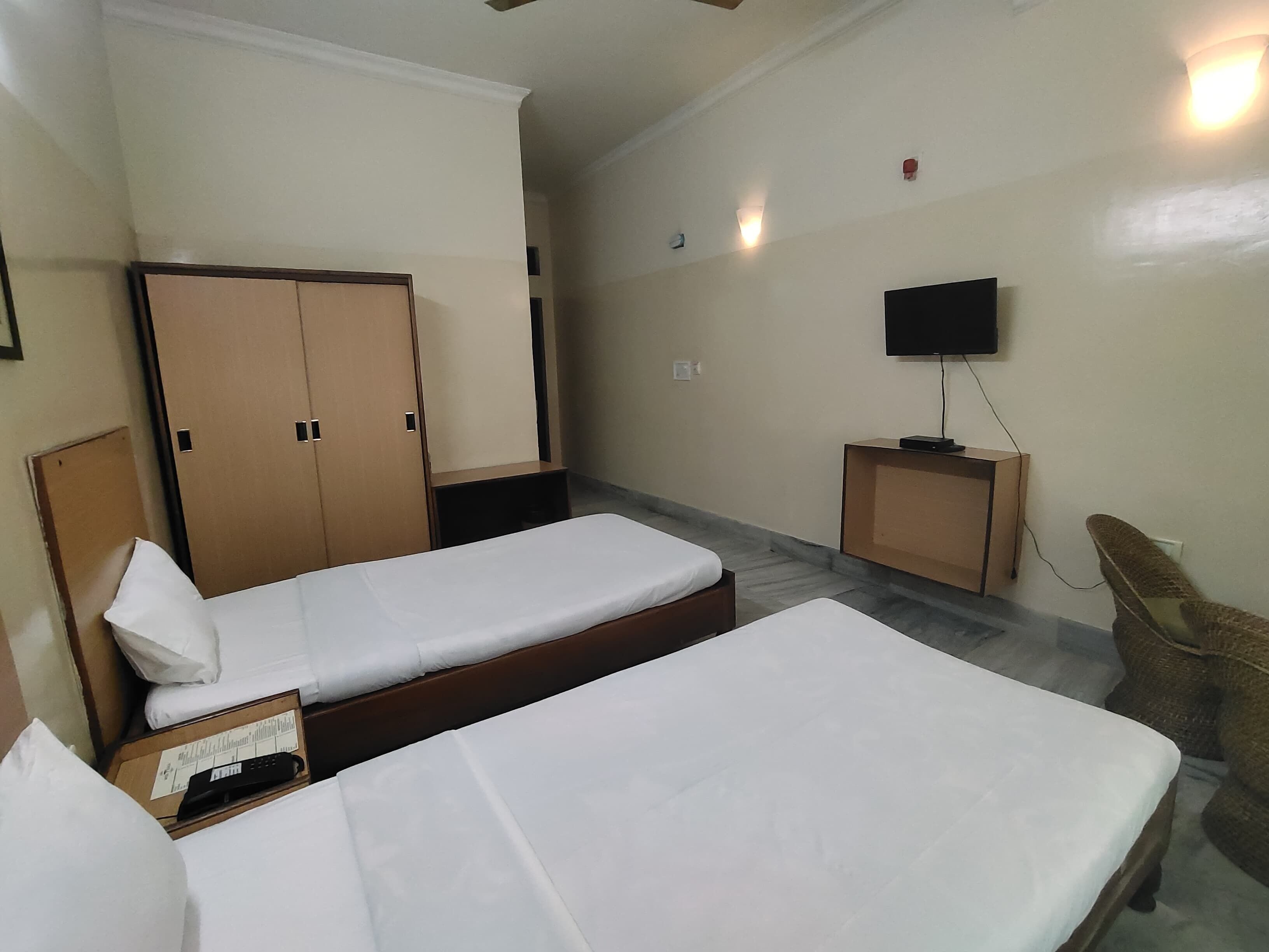 A hotel room with two single beds, a wardrobe, a television, and a small desk.