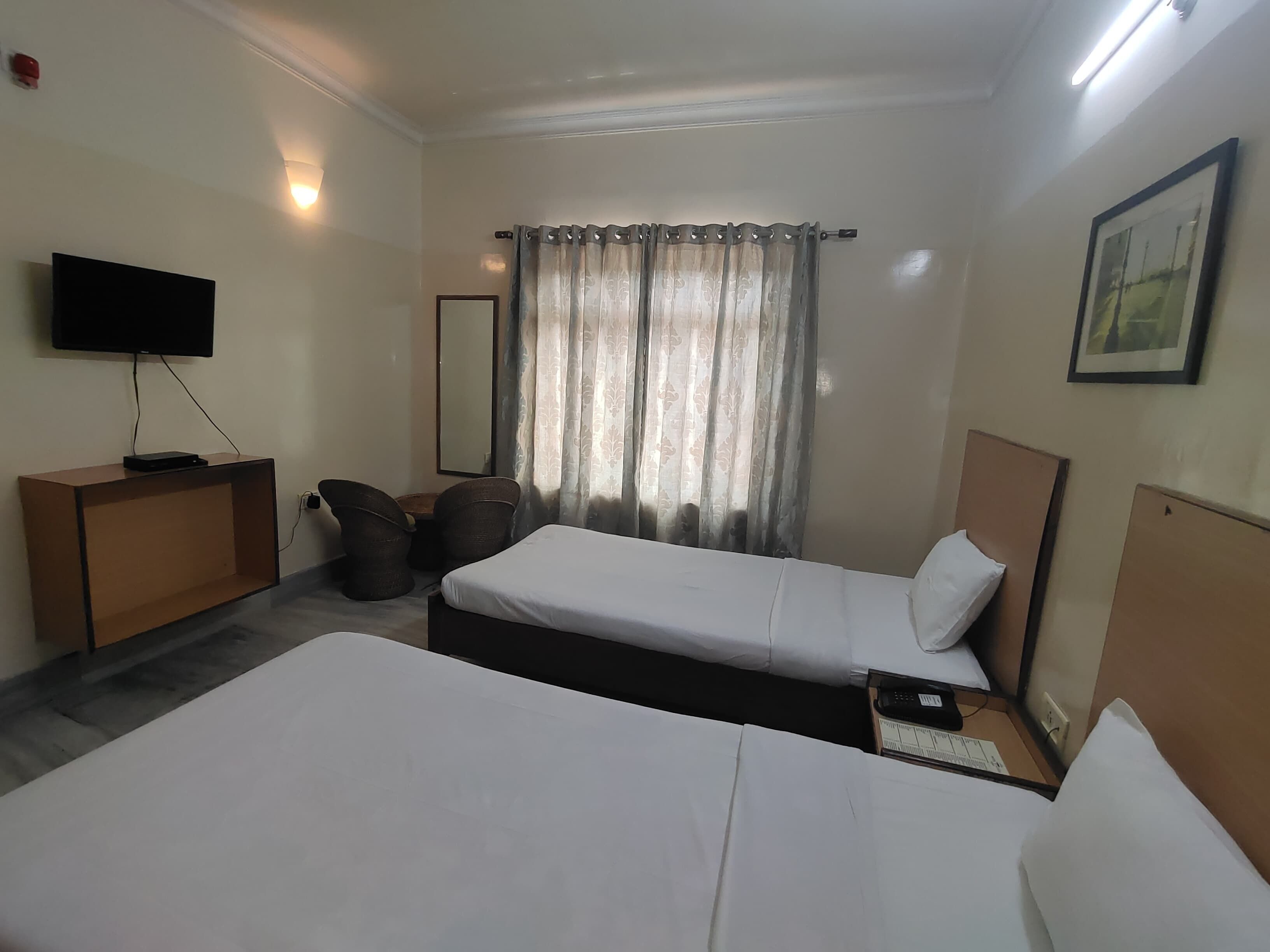Een hotelkamer met twee bedden, een televisie, een bureau en een raam met gordijnen.