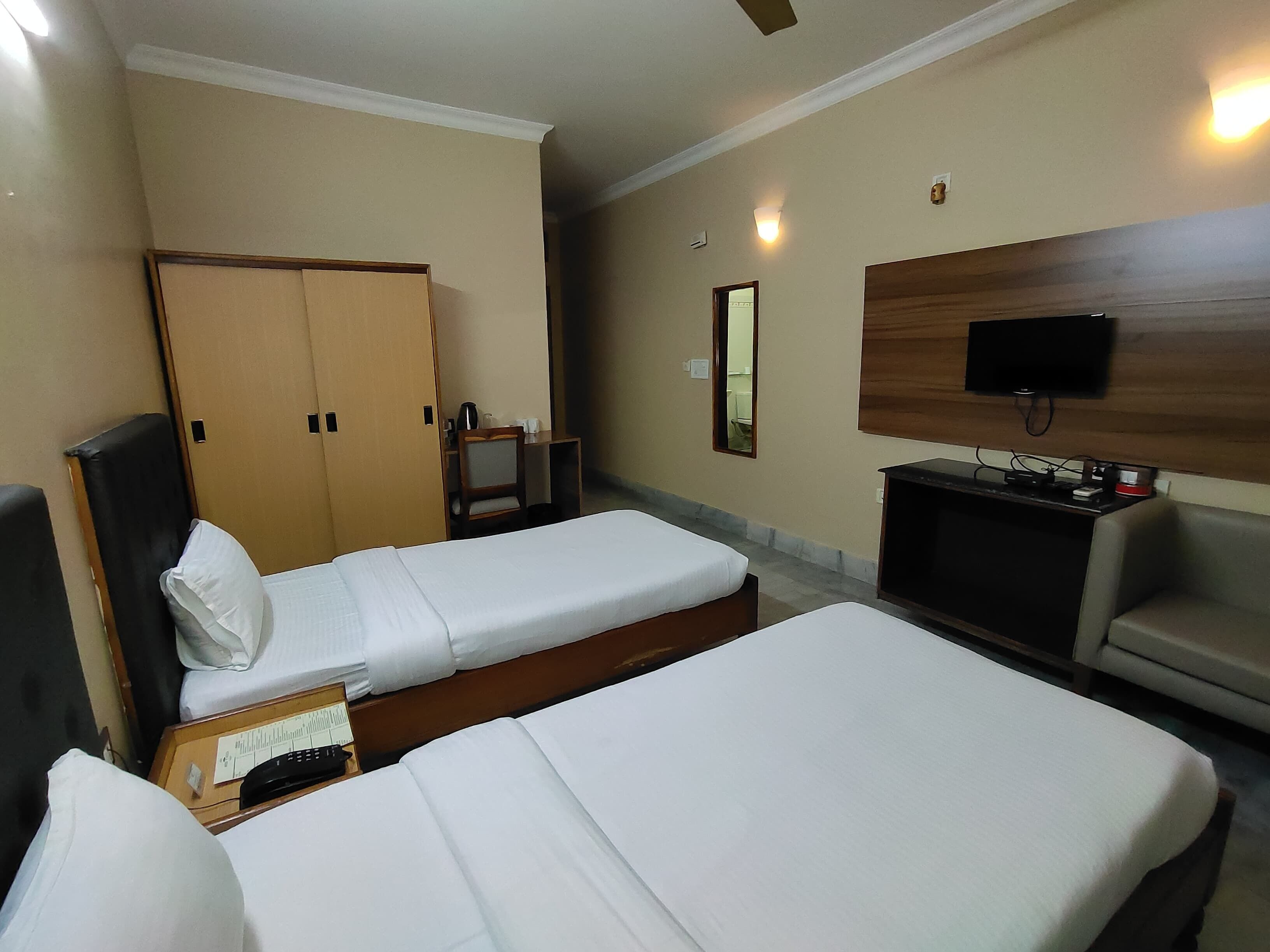 A hotel room with two single beds, a desk with a chair, a TV, and a wardrobe.