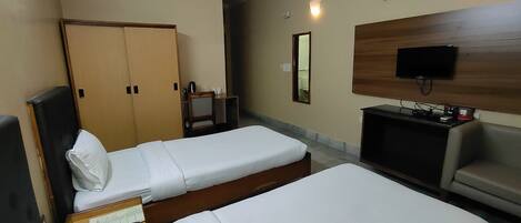 A hotel room with two single beds, a desk with a chair, a TV, and a wardrobe.