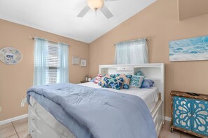 Un dormitorio con cama, ventilador de techo, mesita de noche y un mueble decorativo.