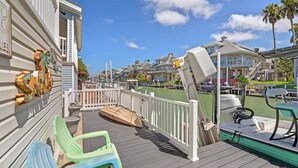 A wooden deck with a boat, a white railing, and a row of houses with balconies. - Long Island Village Pet Friendly 857 (Port Isabel)