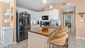 A modern kitchen with white cabinets, stainless steel appliances, and a wooden island with bar stools. - Long Island Village Pet Friendly 857 (Port Isabel)