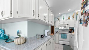 A kitchen with white cabinets, a microwave, an oven, and a refrigerator. There is a decorative pumpkin on the counter. - 307 Long Island Village (Port Isabel)