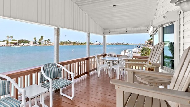 A covered outdoor area with a wooden deck, white chairs, and a table. - 307 Long Island Village (Port Isabel)