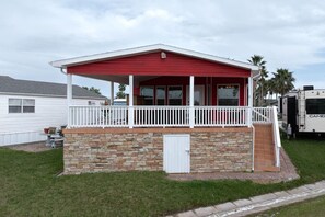 A single-story building with a red roof and white exterior, featuring a small porch with a white railing and a stone foundation.