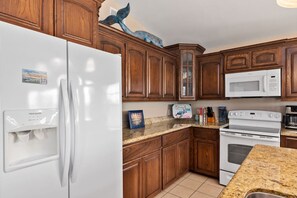 Une cuisine avec des meubles de rangement en bois, un réfrigérateur blanc, un four à micro-ondes et un four traditionnel.