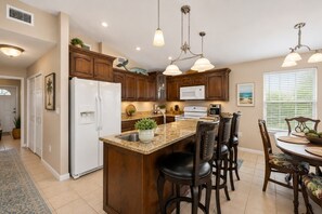A kitchen with wooden cabinets, a white refrigerator, a microwave, a stove, and a bar area with stools.