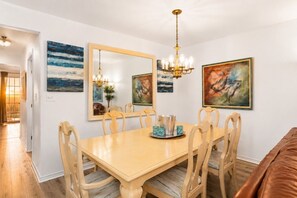 Une salle à manger avec une grande table, des chaises, un lustre et des œuvres d’art accrochées aux murs.